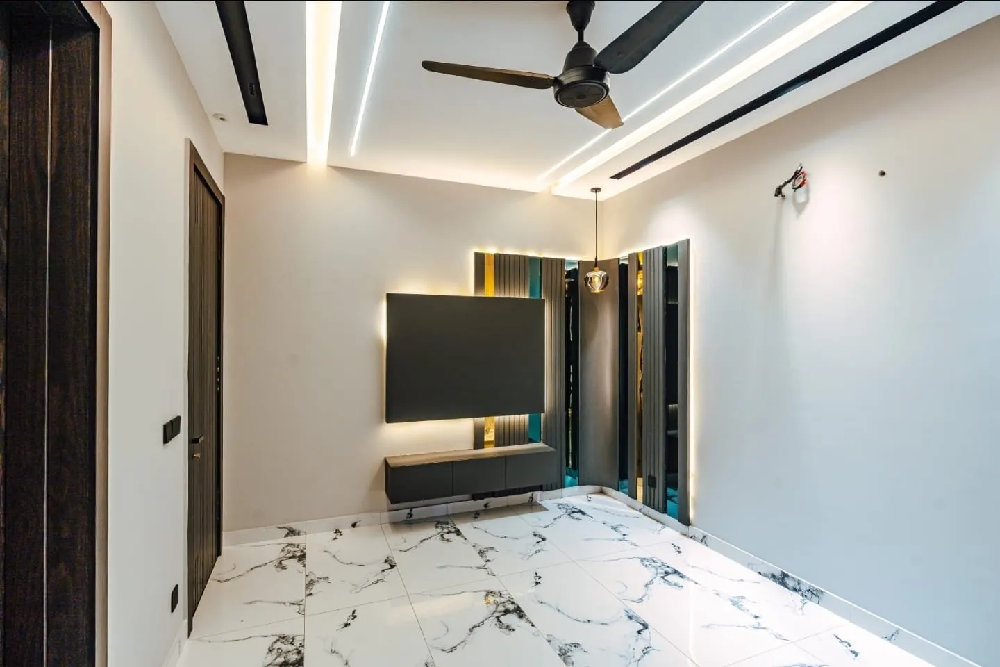 Room with a ceiling fan, TV wall, and white patterned flooring.